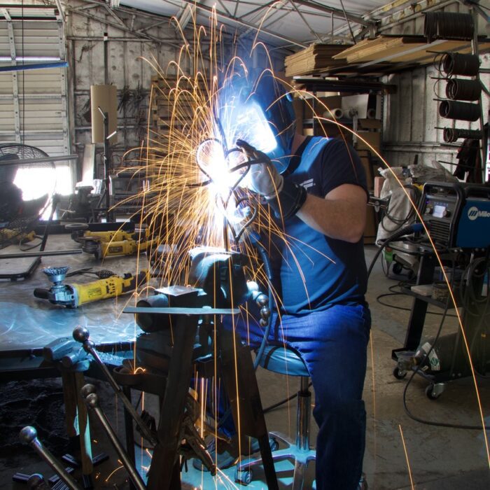 A man welding in a garage with many other machines.