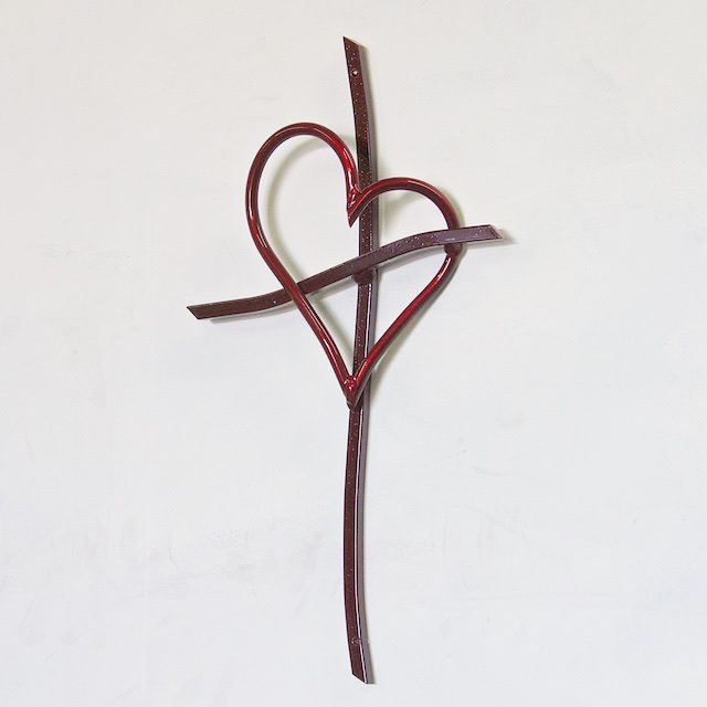 A cross with a heart on it hanging from the wall.