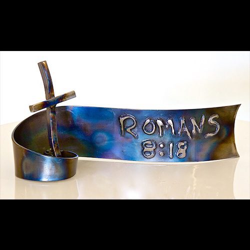 A metal cross with the name of romans 3 : 1 8 on it.