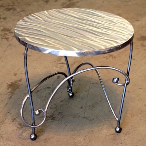 A metal table with a silver top and curved legs.