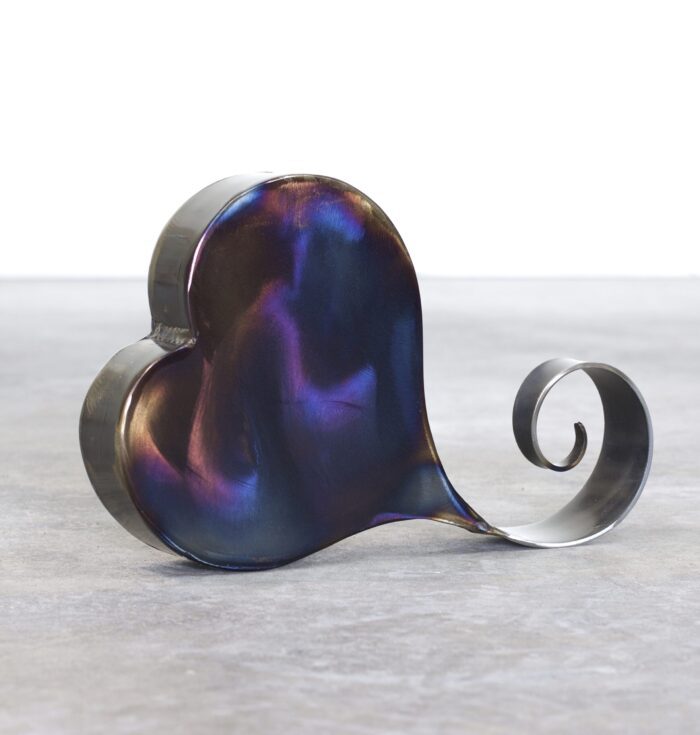 A metal heart with a spiral tail on top of it.