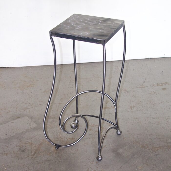 A metal table with a black top and curled legs.