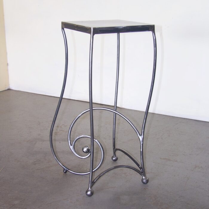A metal table with a black top and swirling legs.