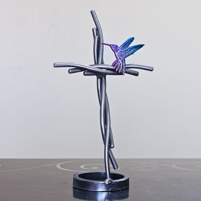 A metal sculpture of a hummingbird on top of a cross.
