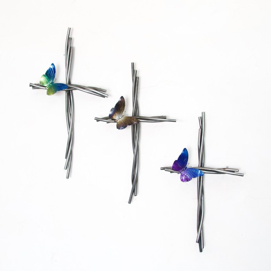 Three butterflies flying above a cross on a white wall.